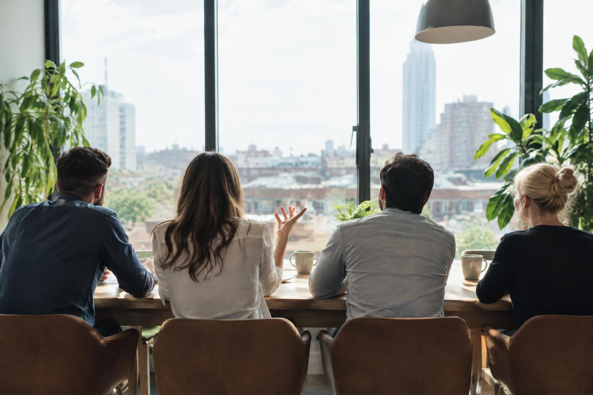 Quatre collègues souriants autour d'une table dans un bureau lumineux